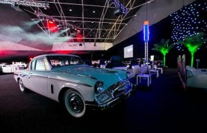 vintage cars inside a ballroom to make it look like a drive in cinema. star cloth wall and palm trees. drive in cinema set inside a ballroom. car cutouts with sofas in front and drive in speakers for guests to watch movies