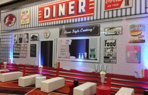 large 12m diner backdrop with image of diner wall. white bench seats, milkshake centrepieces and tables with record tops in front