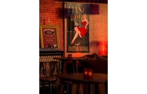 cocktail bar with posters on faux brick wall. orange velvet sofas and wooden hi bars and stools in front