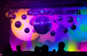 varying sizes of mirror balls from 200mm to 1m hanging at different heights from a ceiling truss with large av screen in background