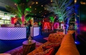 arabian nights themed cocktail party at frasers restaurant perth. Large illuminated white and gold circular bar in centre of room with 4m palm trees. orange velvet sofas with arabian cushions