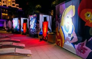 alice in wonderland themed party poolside at Crown perth. Alice themed backdrops hanging from cabanas with lighting behind and card soldier props
