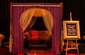 arabian nights themed photo booth with velvet sofas and low wooden table with arabian rug. custom made sign on easel