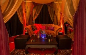 arabian nights themed booth hut with velvet sofa, wooden table and arabian themed cushions and silk drapes