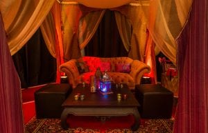 arabian nights themed photo booth with silk drapes, orange velvet sofa, low table and persian arabian rug