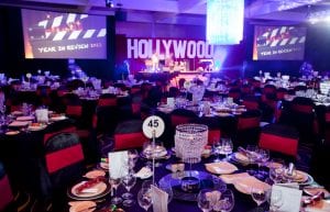 Hollywood event theme with crystal chandelabra centrepieces, red chair bands, black chair covers, red drapes and large Hollywood prop for hire.