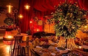 Steam Punk event theme with red drapes, large gold frames, steam punk prints, crystal beaded chandeliers, lanterns, velvet sofas, cushions, cow print rugs, birdcages, coffee tables, Edison globes, greenery, gobos, cloche dome centrepieces, trussing, hi bar takes and stools for hire.