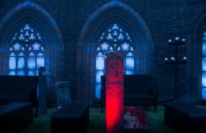 Rocky Horror event theme with coffin coffee table, gothic window drape backdrop, hi back sofas, rectangular ottomans, candelabra, parcan lights, skeletons and cemetery props for hire.
